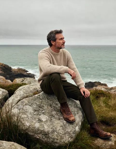 Mann im Strickpullover auf einem Felsen am Meer